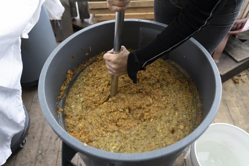 Deirdre Heekin, the owner of the La Garagista winery, mixes apple mash in a large plastic canister, in Barnard, Vt., Oct. 26, 2023. A growing number of producers are fermenting grapes, apples and other fruits together, or blending wine and ciders, to make fascinating beverages. (Kelly Burgess/The New York Times)