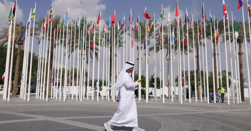 A man wearing a thawb walks past flags of nations participating in the UNFCCC COP28 Climate Conference the day before its official opening on November 29, 2023 in Dubai, United Arab Emirates.