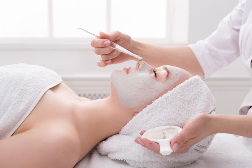 Face peeling mask, spa beauty treatment, skincare. Woman getting facial care by beautician at spa salon, side view, close-up