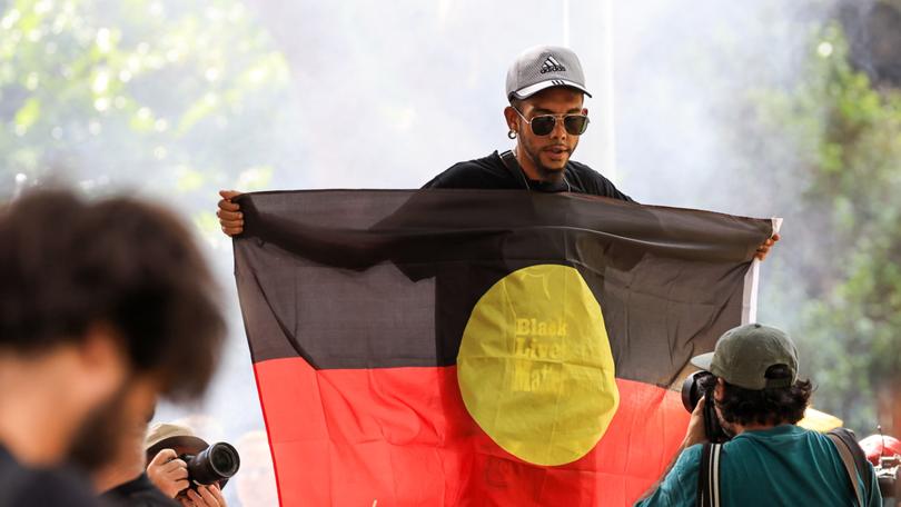 A man holds up the Aboriginal flag during an Invasion day rally at Belmore Park on January 26, 2024 in Sydney, 