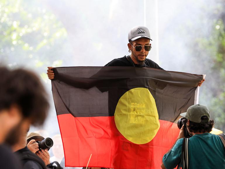 A man holds up the Aboriginal flag during an Invasion day rally at Belmore Park on January 26, 2024 in Sydney, 