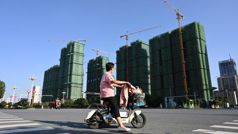 A woman rides a scooter past the construction site of an Evergrande housing complex in Zhumadian, central China’s Henan province on September 14, 2021. (Photo by JADE GAO / AFP)