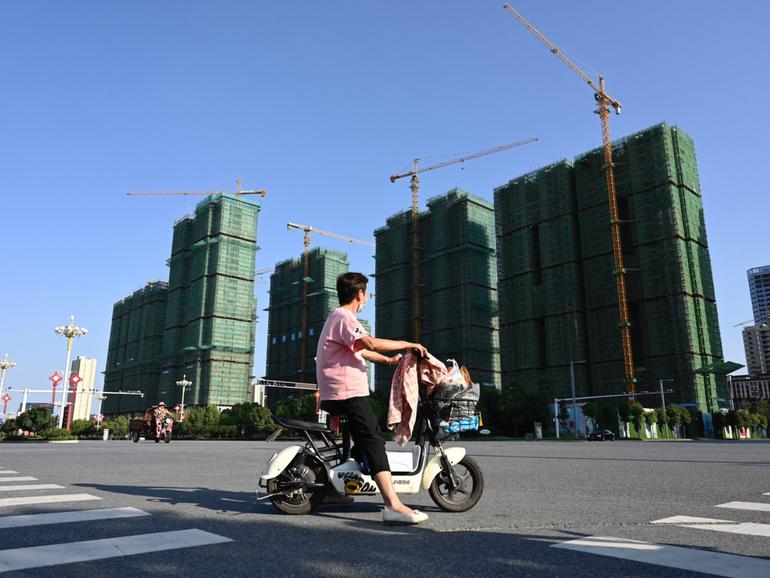 A woman rides a scooter past the construction site of an Evergrande housing complex in Zhumadian, central China’s Henan province on September 14, 2021. (Photo by JADE GAO / AFP)