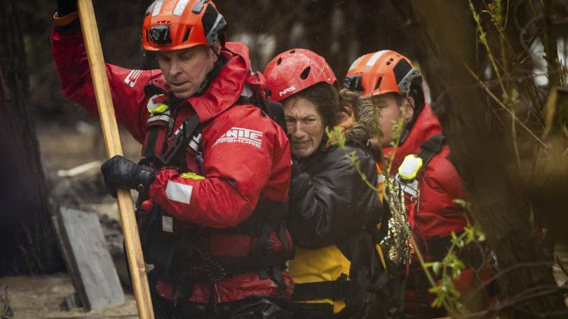 Firefighters rescue a woman from a homeless encampment that became surrounded by floodwater.