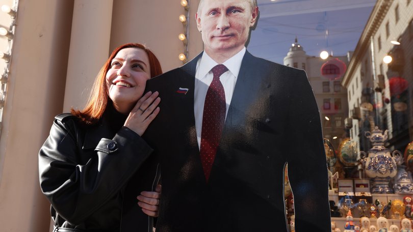 A woman poses for a photo beside a full-length cardboard cut-out of President Vladimir Putin as the country heads to the polls.