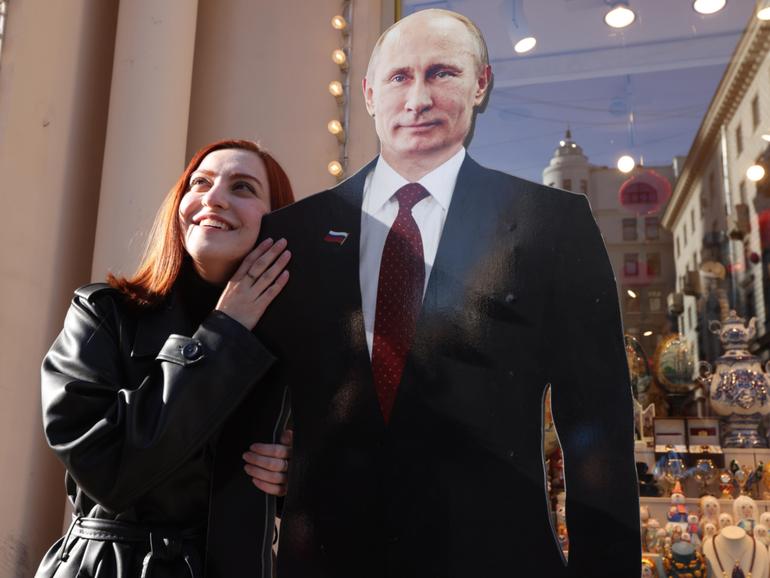 A woman poses for a photo beside a full-length cardboard cut-out of President Vladimir Putin as the country heads to the polls.