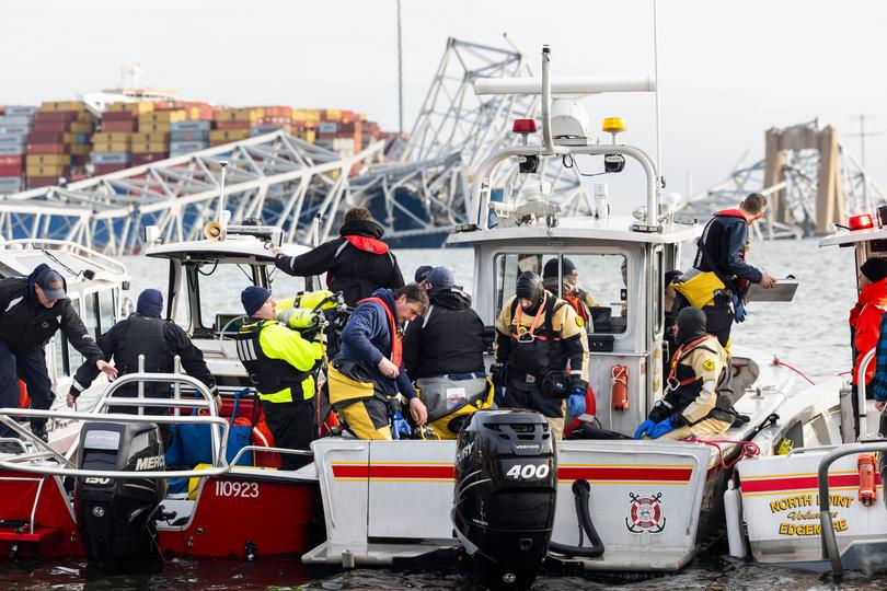 Rescue personnel gather on the shore of the Patapsco River after a container ship ran into the Francis Scott Key Bridge (back) causing its collapse in Baltimore.