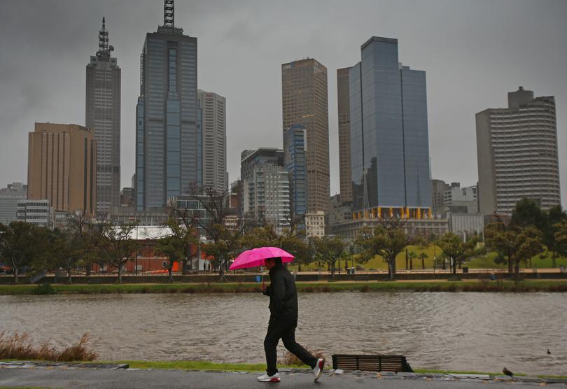 A man shelters from the rain under an umbrella as he walks along the Yarra River in Melbourne.