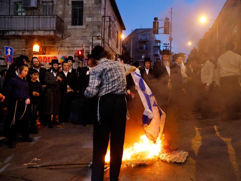 An ultra-orthodox jew burns an Israeli flag as anti-government protests are stepped up.