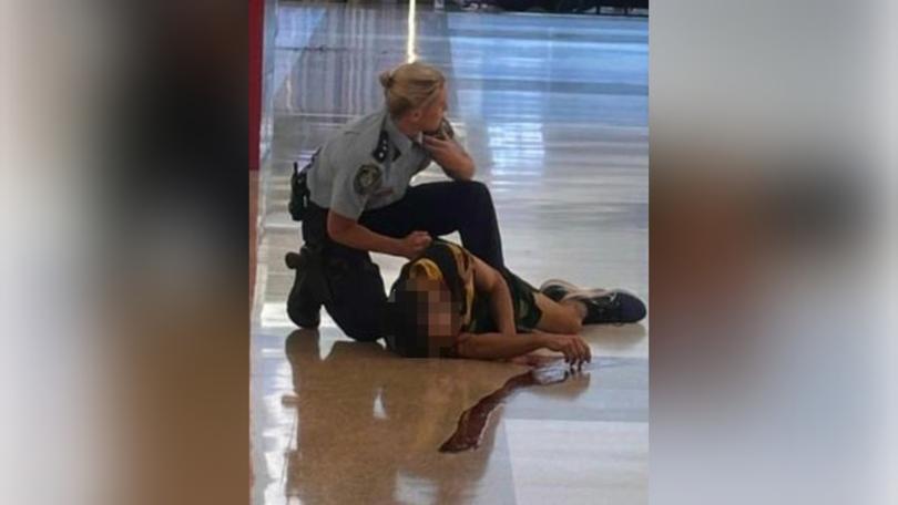 A police officer talks on their radio as a wounded man lies on the floor of Bondi Junction.