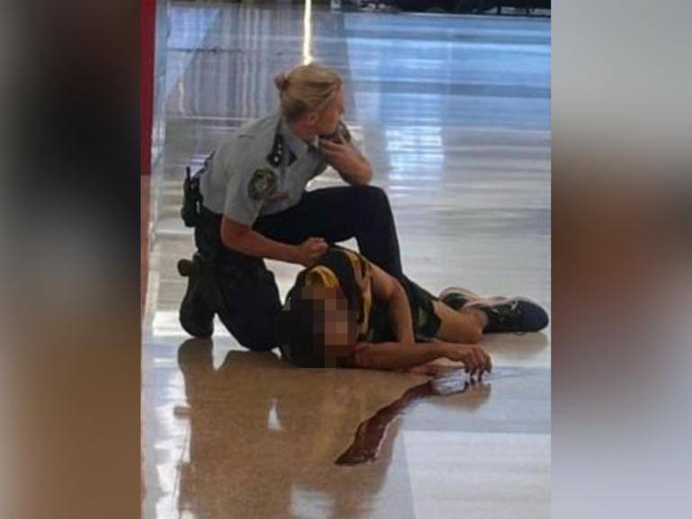 A police officer talks on their radio as a wounded man lies on the floor of Bondi Junction.