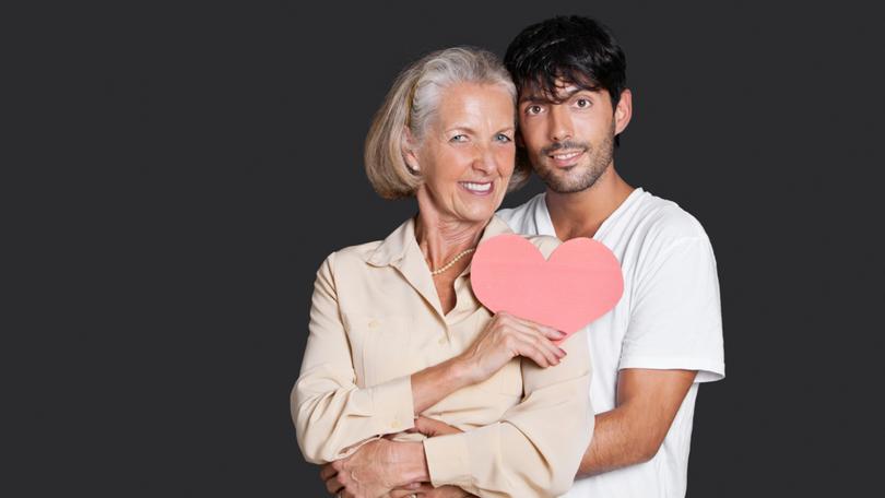 Young man embracing senior woman holding red paper heart against black background