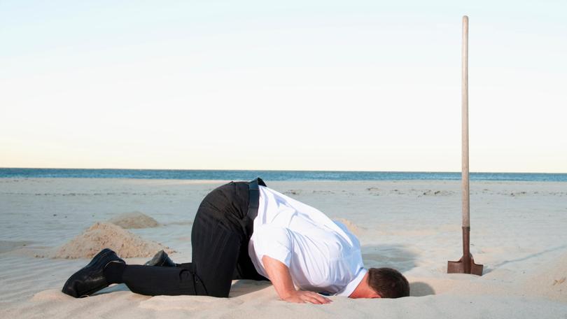 Caucasian businessman burying head in sand Jacobs Stock Photography Ltd