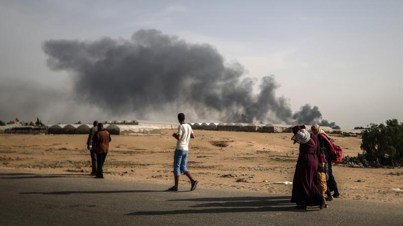 Palestinians walk past after tents in Al-Mawasi, previously declared as a 'safe zone' by Israel, burn in the city of Rafah.