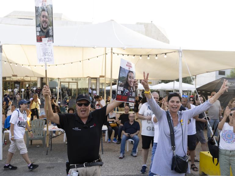 People celebrate as they hold photos of released hostages Noa Argamani and Almog Meir Jan at Tel Aviv's square.