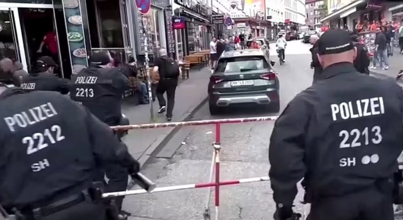 Police have neutralised a suspect with an axe near a fan complex at the famous Reeperbahn in Hamburg, where thousands of fans are gathering today due to the match between the national teams of Holland and Poland.
PICTURED: He turns his back as he is doused in pepper spray and runs up the street as passers-by scurry across the road