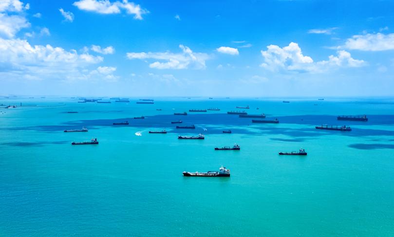 Aerial view of cargo, freight or container ships in the road in Singapore Strait. Blue sky, beautiful clouds, azure clear sea waters. Cargo ships anchored and waiting to enter the busiest port in South East Asia. Copyspace. International trade. Natallia Pershaj