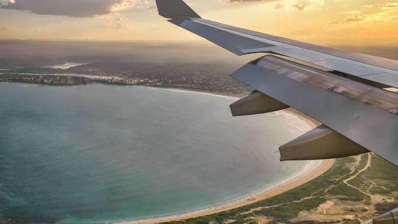 Airplane wing seen from airplane window approaching Sydney, Australia, at sunset.