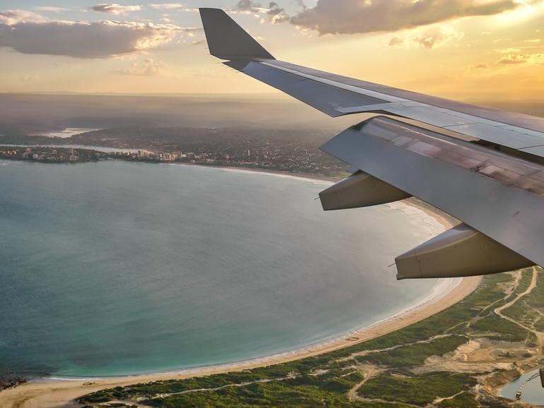 Airplane wing seen from airplane window approaching Sydney, Australia, at sunset.