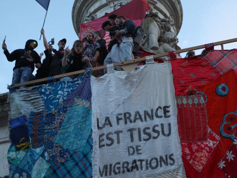 Participants gesture as they stand with a giant banner which reads as “France is the fabric of migration” during an election night rally following the first results of the second round of France’s legislative election, at Place de la Republique in Paris on July 7, 2024.