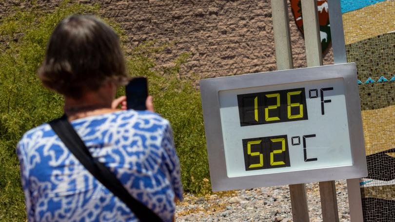 A woman takes a photo of a thermostat reading 126 degrees Fahrenheit and 52 degrees Celsius at the Furnace Creek Visitors Centre in Death Valley.