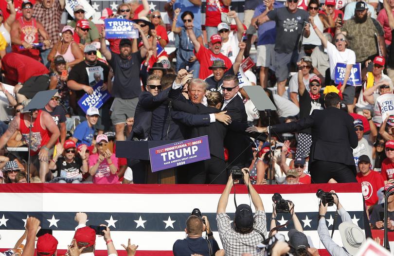 President Donald Trump pumps his fist as he is rushed from the stage by secret service agents. 