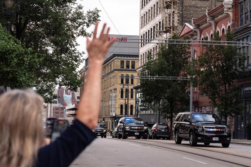 A woman waves toward a motorcade ahead of the 2024 Republican National Convention in Milwaukee.