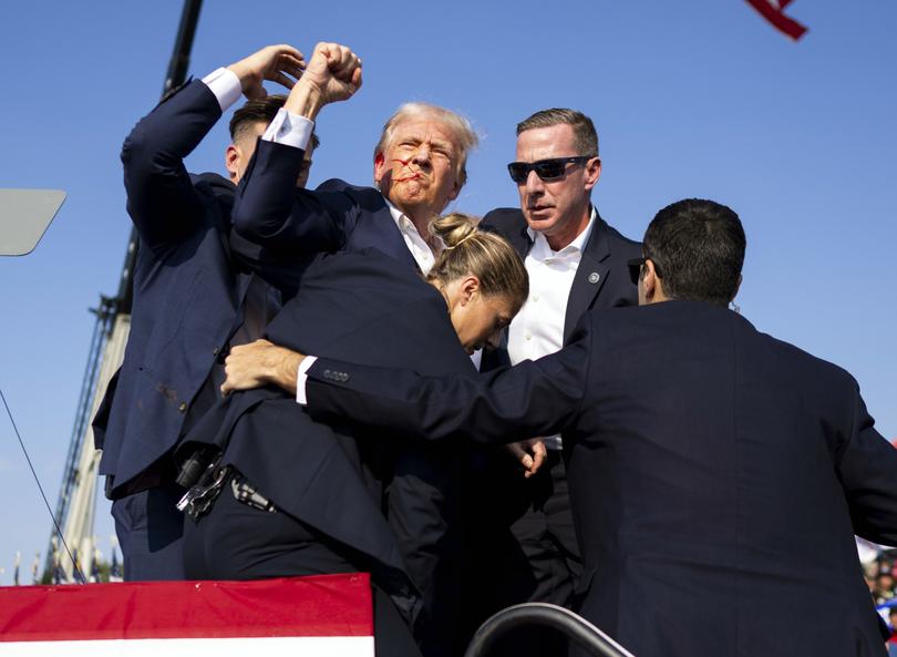 A bloodied Donald Trump is surrounded by Secret Service agents before being spirited away after shots were fired.