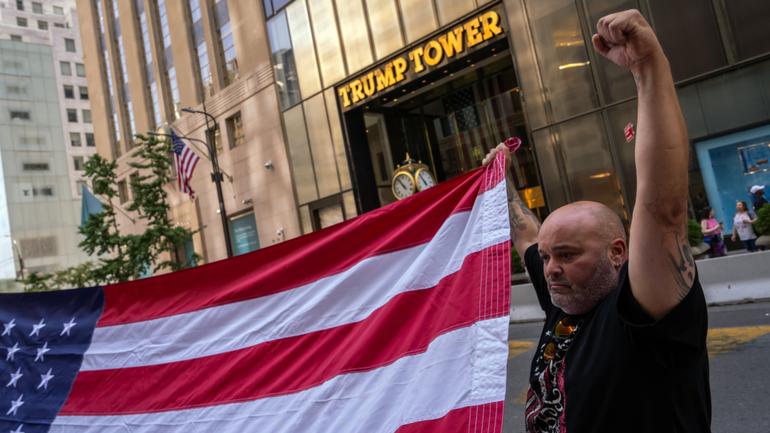 A supporter of former President Donald Trump helps to unfurl an oversized United States flag outside Trump Tower in midtown Manhattan on Sunday morning, one day after Trump was shot while speaking at a campaign rally.