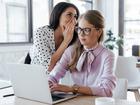 businesswoman whispering in ear of coworker in glasses while gossiping in office