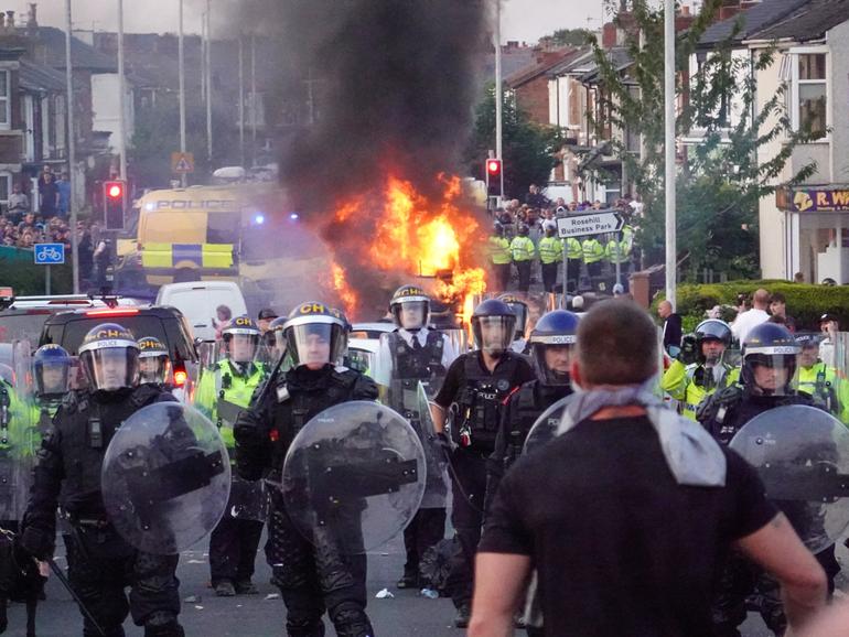 Riot police hold back protesters near a burning police vehicle after disorder broke out in Southport, England. 