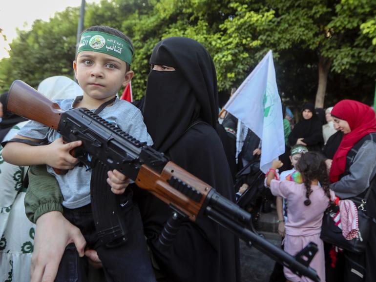 A supporter of the Islamist Hamas movement carries her son, who holds a toy machine gun during a protest in the southern port city of Sidon, Lebanon, 