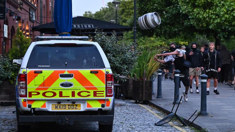 A rioter throws a beer keg at a police car in Bristol during the 'Enough is Enough' demonstration held in reaction to the fatal stabbings in Southport.