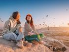 Girl friends sitting on a clifftop viewpoint and admiring view of majestic flying hot air balloons in Cappadocia