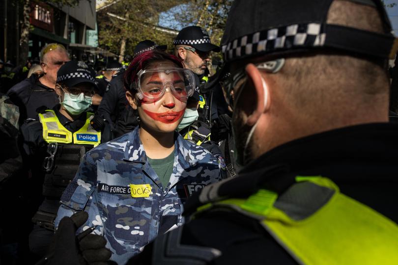 Members of Victoria Police detain a protester wearing a uniform of the Australian Airforce for a bag search.