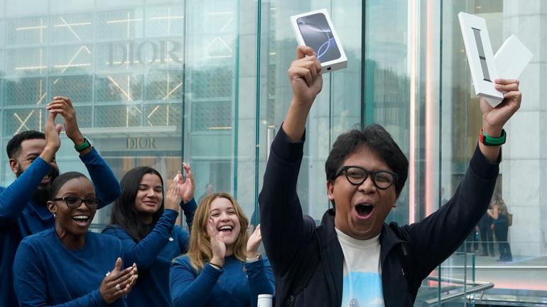 Apple employees applaud as a customer celebrates their purchase of Apple's iPhone 16 launch in New York.