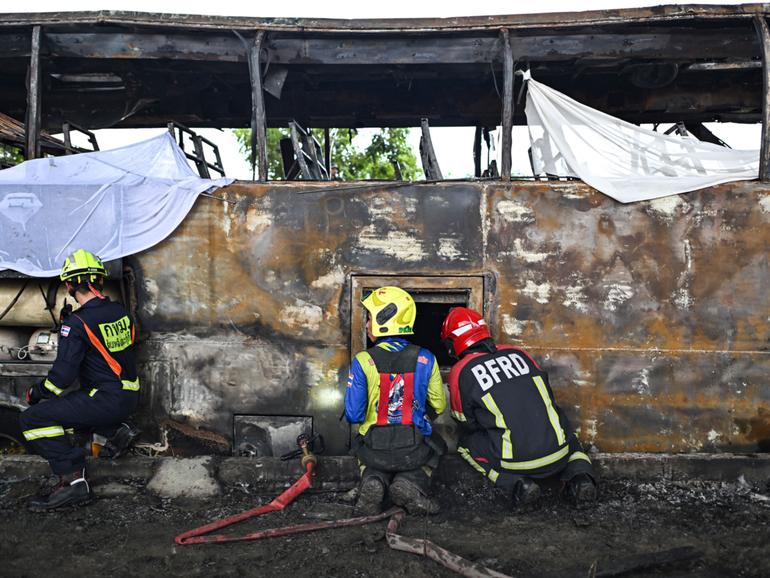 Firefighters and rescue workers stand next to a burnt-out bus that was carrying students and teachers on the outskirts of Bangkok, on October 1, 2024.