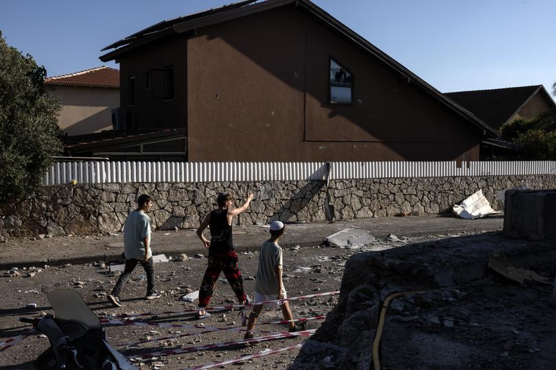 Israeli teenagers walk by a home that was hit by a rocket fired from Lebanon, causing it to burst into flames, in Safed, Israel, last month. 