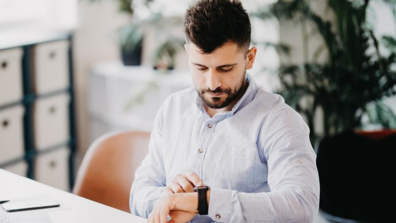 Handsome young man setting smart watch while sitting at the desk in creative office