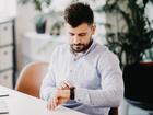 Handsome young man setting smart watch while sitting at the desk in creative office