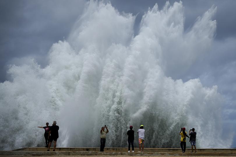 People take photos of the spray from waves crashing against the Malecon seawall.