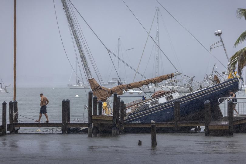 People inspect a stranded sailboat at the Marina Jack as the town prepares for Hurricane Milton in Oyster Bay, Sarasota, Florida.