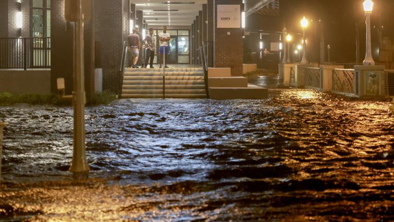 People look out at surge waters flooding the street from their building after Hurricane Milton came ashore in the Sarasota area in Fort Myers, Florida.