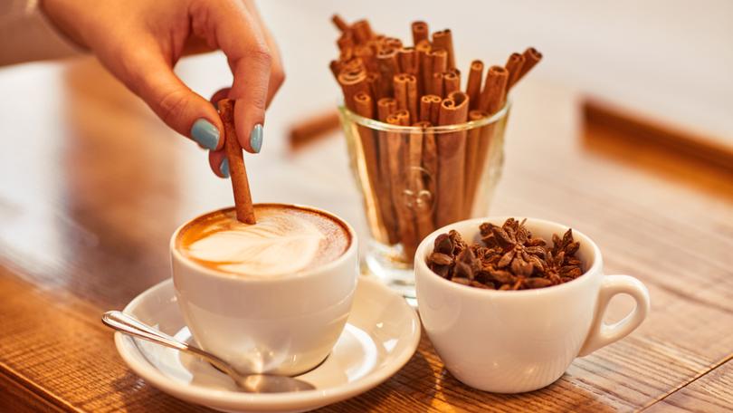 Add some flavor. Close up of hand of nice woman holding stick of cinnamon and putting it into cup of coffee 