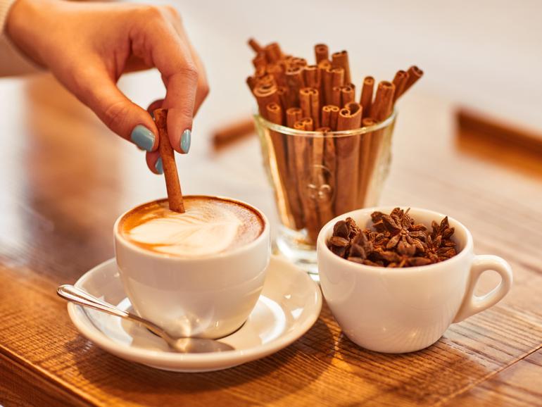 Add some flavor. Close up of hand of nice woman holding stick of cinnamon and putting it into cup of coffee 