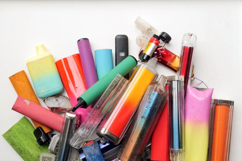 A collection of discarded electronic cigarette vapes and internal components shot over a white plastic background.