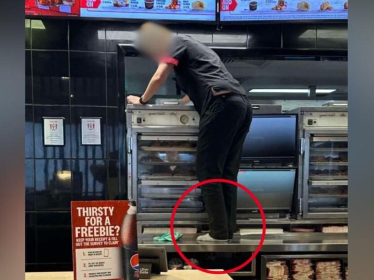 A photo shows a KFC worker in Queensland had climbed onto a countertop to clean an appliance.