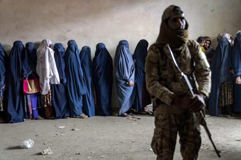 A Taliban fighter stands guard as women wait to receive food rations distributed by a humanitarian aid group, in Kabul, Afghanistan, Tuesday, May 23, 2023.