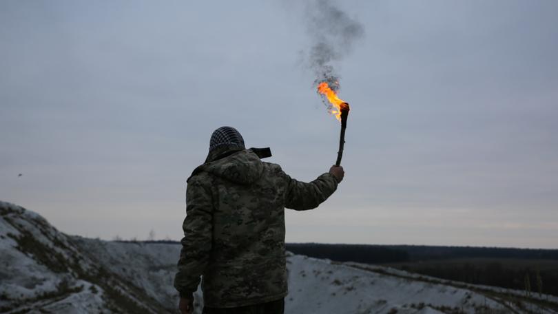 Soldier is holding torch with fire. Man in camouflage uniform and checkered keffiyeh shemagh bandana. Terrorist in the mountains gorge. War concept. White hills and dry grass in the desert.