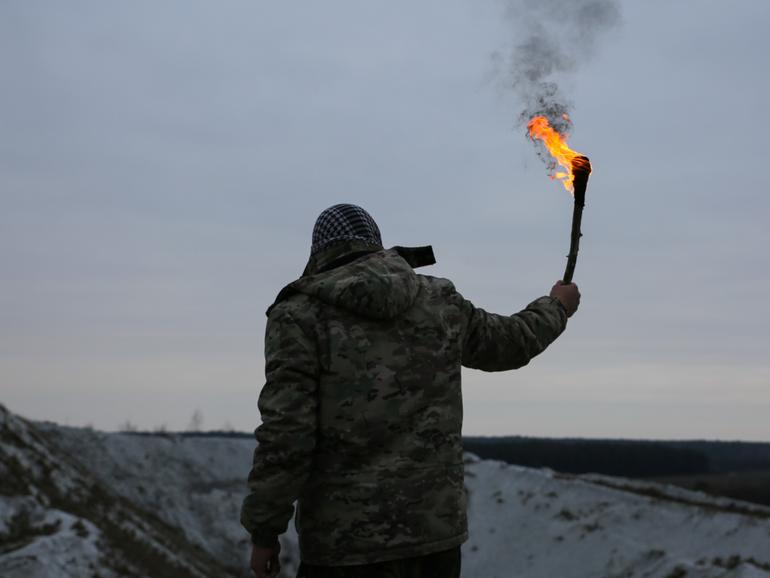 Soldier is holding torch with fire. Man in camouflage uniform and checkered keffiyeh shemagh bandana. Terrorist in the mountains gorge. War concept. White hills and dry grass in the desert.